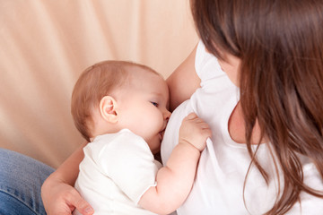 A young woman feeds the baby's chest, sitting on the bed
