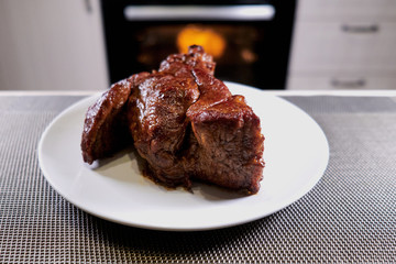 Huge piece of meat on plate. Roast beef close-up. Barbecue meat in modern kitchen. Blurred background oven. Hot cooked dinner. Huge steak on a white plate.