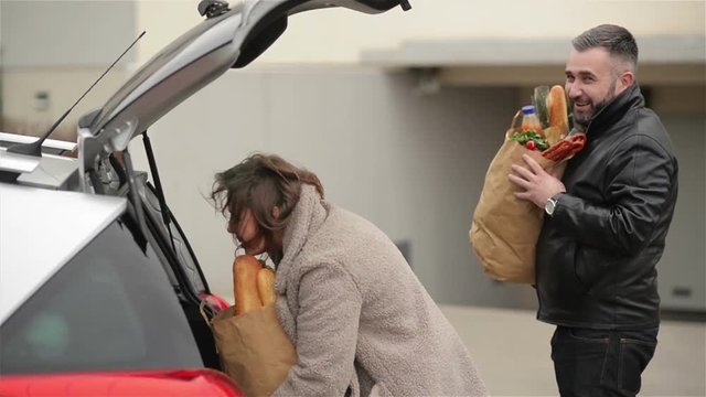 Young Family Is Packing Her Groceries Bags To New Car. Front View Of Handsome Bearded Man And Beautiful Woman.
