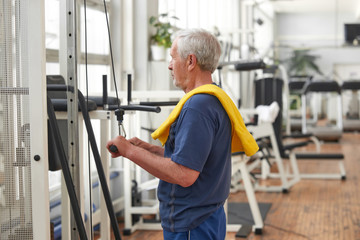 Fototapeta na wymiar Elderly man exercising at gym. Senior caucasian man working out at gym using cable equipment. Sport for good health.