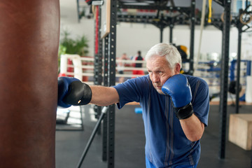 Male pensioner trains on a punching bag. Serious older man working out with punching bag at boxing...