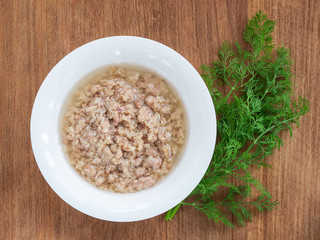 White porcelain bowl with shredded tuna in oil for cooking salad and green dill on a wooden background. Seafood, healthy eating and cook at home concept.
