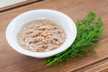 Porcelain bowl with shredded tuna in oil for cooking salad and green dill on a wooden background. Seafood, healthy eating and cook at home.