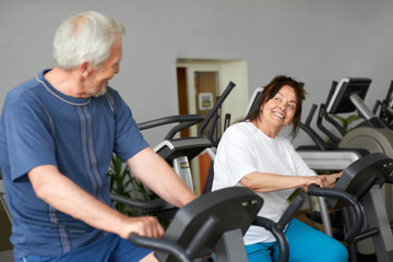 Fototapeta na wymiar Beautiful couple of seniors working out at gym. Elderly man and woman training on machine at fitness club, focus on woman. Aged people doing cardio workout.