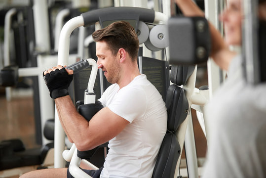 Handsome muscular man in gym doing exercises. Caucasian male taking efforts to finish set on chest press. Regular sport training for perfect shape.