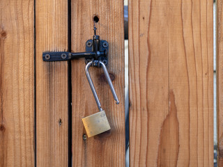 Unlocked lock hanging on a latch on a redwood fence.