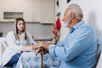 Young positive caregiver taking care of senior man in nursing home