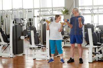 Fototapeta na wymiar Happy senior couple lifting dumbbells at gym. Elderly couple exercising in gym and looking at each other. People, sport, leisure, positive emotions.