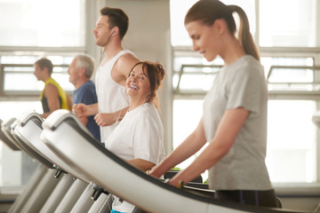 Senior woman on treadmill smiling at camera. People exercising at modern sport club. People, fitness, active lifestyle.