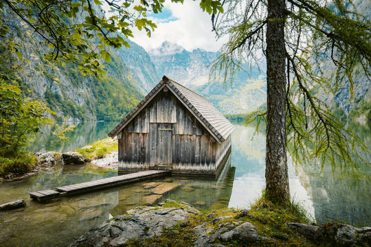 Idyllic view of traditional old wooden boat house at scenic Lake Obersee on a beautiful sunny day with blue sky and clouds in summer, Nationalpark Berchtesgadener Land, Bavaria, Germany