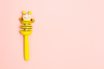 Yellow wooden baby toy with bells. Traditional rattle on pink background. Overhead view. Copy...