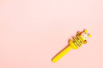 Baby wooden rattle with metal bells for small child. Yellow toy on pink background with copy space. Flat lay style