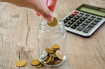 female hand throwing a coin in a jar against the background of a calculator
