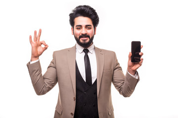 Portrait of arab handsome business man posing holding mobile phone showing okay gesture isolated over white background