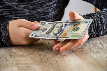 Female hands hold one hundred dollar bills on the background of the table.