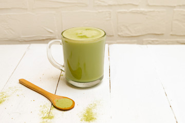 A cup of matcha latte green tea and wooden spoon with matcha powder on white background, copy space