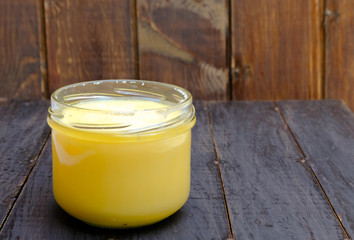Ghee butter or clarified butter in a jar on wooden background, copy space