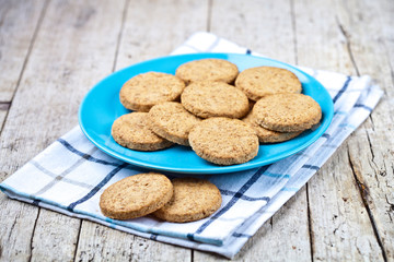 Fresh baked oat cookies on blue ceramic plate on linen napkin on rustic wooden table.