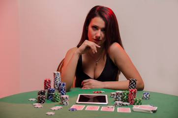 cute girl sitting at poker table, tablet in front of her, online poker concept 