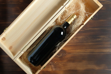 A dark expensive bottle of wine in a wooden box on a wooden background.