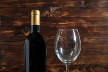 A dark bottle of wine next to glass goblet on a wooden background.