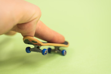 Fingerboard. Man make trick by two fingers with small skateboard on green background. © gesrey