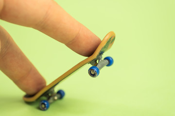 Fingerboard. Man playing by two fingers with small skateboard on green background. © gesrey