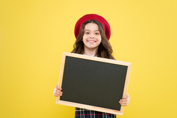 small girl in french beret. advertisement. child with empty blackboard. parisian child on yellow background. happy girl with curly hair in beret. your advertisement in good hands. advertisement board