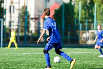 Obraz premium Junior football match. Boys in blue white sportswear play soccer match on football pitch. Football stadium, grass field at the background Soccer for young players. Training, sport, activity outdoor