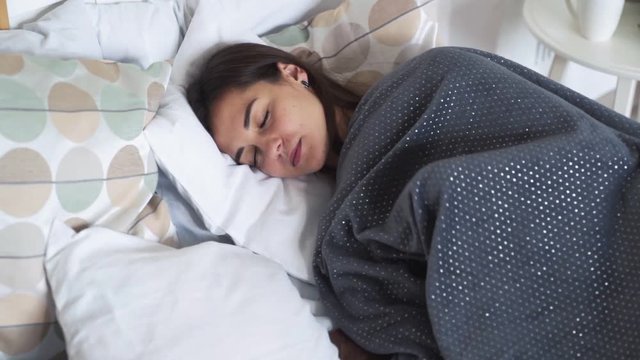 Woman sleeps quietly in her bed, wrapped in blankets during dreams, slow motion