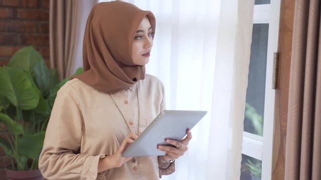 portrait of muslim smart woman with tablet pc standing near window
