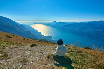 Fototapeta premium Nice little child admiring the beautiful Lake Garda from Monte Baldo, Panorama of the gorgeous Garda lake surrounded by mountains