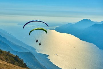 Paraglider flying over the Garda Lake,Panorama of the gorgeous Garda lake surrounded by mountains, Malcesine,Italy - obrazy, fototapety, plakaty