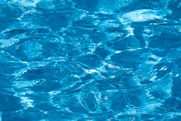 Blue and bright ripple water surface in swimming pool with sun reflection.