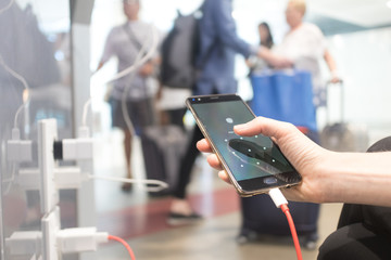 Female hands holding and using smartphone while charging it in a public place using electric plug...
