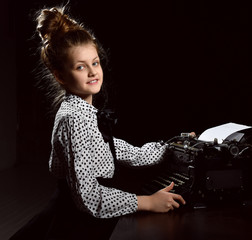 Pretty little girl kid typing letter on vintage typewriter keyboard machine on dark 