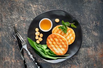 Grilled round slices of Greek cheese with honey, fresh mint and coriander leaves. Flat lay on dark grey table