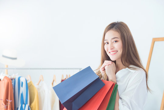 Beautiful asian woman holding shopping bags and smiles at garments apparel clothing shop. Sale,Shopping concept .