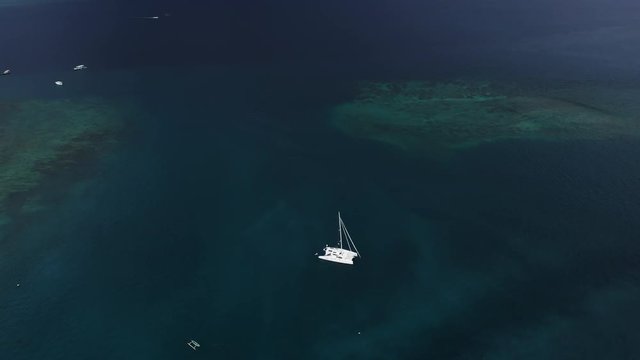 HIGHT angle shot, Top view of the boat. Aerial View of a Anchored Catamaran Yacht Standing and people can Sunbathing on it's Deck. Runabout or cruiser stands in azure Sea Waters With Coral Reef