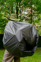 Garbage collection. Man carries a big black trash bag.