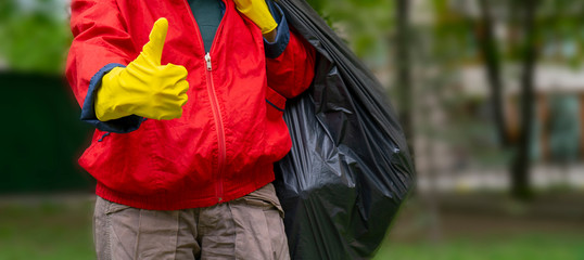 Garbage collection. Man in red coat and yellow gloves showing thumb up, carries a big black bag...