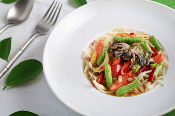 Papaya salad crab Thai food in a white plate on a white wood floor
