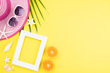 Beach accessories picture frame, sunglasses, starfish, beach hat and Green tropical leaves on yellow background for summer holiday and vacation concept.