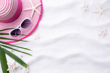Beach accessories Green tropical leaves with sunglasses, flip flop starfish, beach hat and sea shell on white sand beach background for summer holiday and vacation concept.