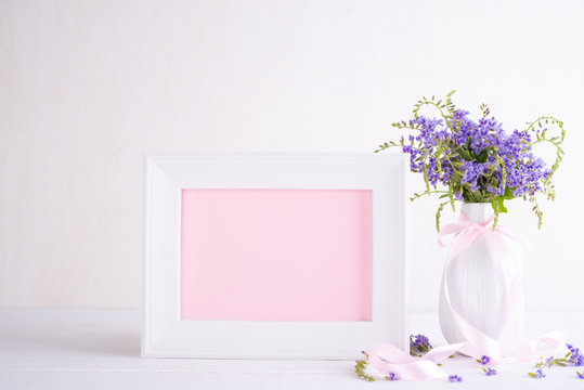 White picture frame with lovely purple flower in vase on white wooden table.