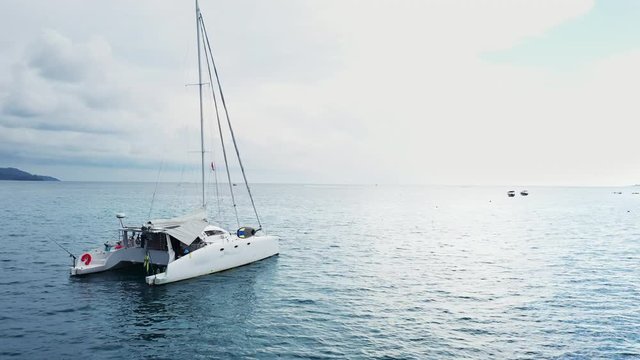 Top view of the boat. Aerial View of a Anchored Catamaran Yacht Standing and people can Sunbathing on it's Deck. Runabout or cruiser stands in azure Sea Waters With Coral Reef Visible. Weekender from