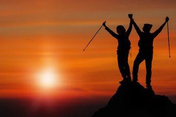 silhouette of two friends having achievement climbing up mountain to the peak together with background of sunrising