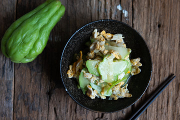 Fresh chayote fruits (Sechium edulis) stir fried with egg and garlic in bowl on wood background