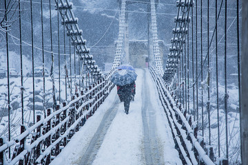 heavy winter snow fall, a person walking alone with black umbrella on the bridge, wide angle shot -...