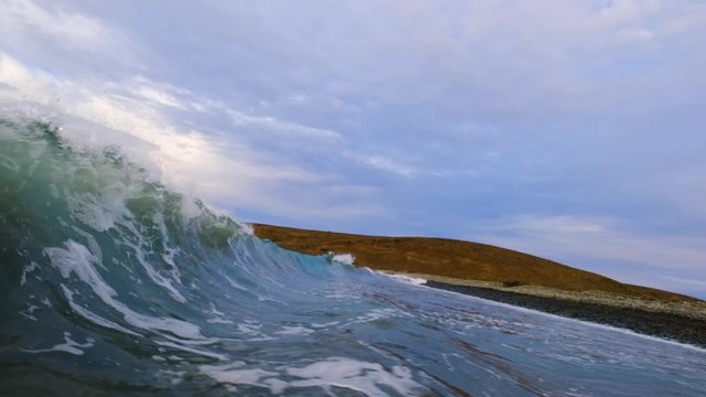 Wave backwash causes unexpected huge round tubular splash over camera.  5x slow motion shot at 120 frames per second and cloudy stormy skies add to the drama.